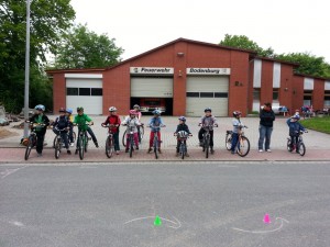 Regnet es oder nicht? Geht die Fahrradtour an? Die Telefone klingelten bei uns Betreuern ohne Unterbrechung. Wir gingen erst einmal von trockenem Wetter aus. Angesichts der anhaltenden dunklen Wolkendecke, blieben wir am Feuerwehrhaus und zeichneten einen Fahrradparcour auf die abgesperrte Straße. Schlangenlinien, Kreise, Engstellen, anhalten und wieder anfahren wurden geübt.